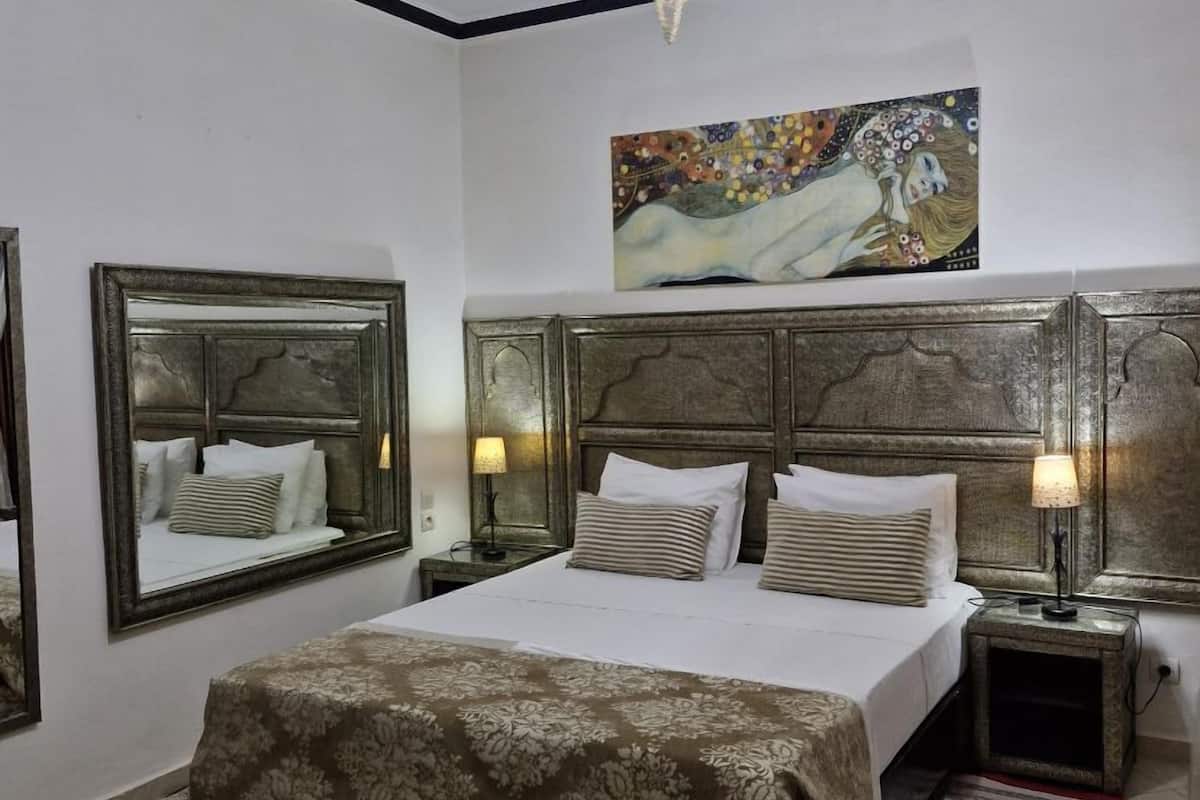 Une chambre à coucher avec un grand lit, deux tables de chevet avec des lampes, un lustre, un tableau au-dessus du lit et un miroir sur le mur.