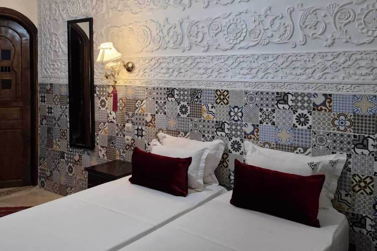 Une chambre d’hôtel avec un grand lit, une table de chevet, une lampe et un mur décoratif orné de motifs complexes.