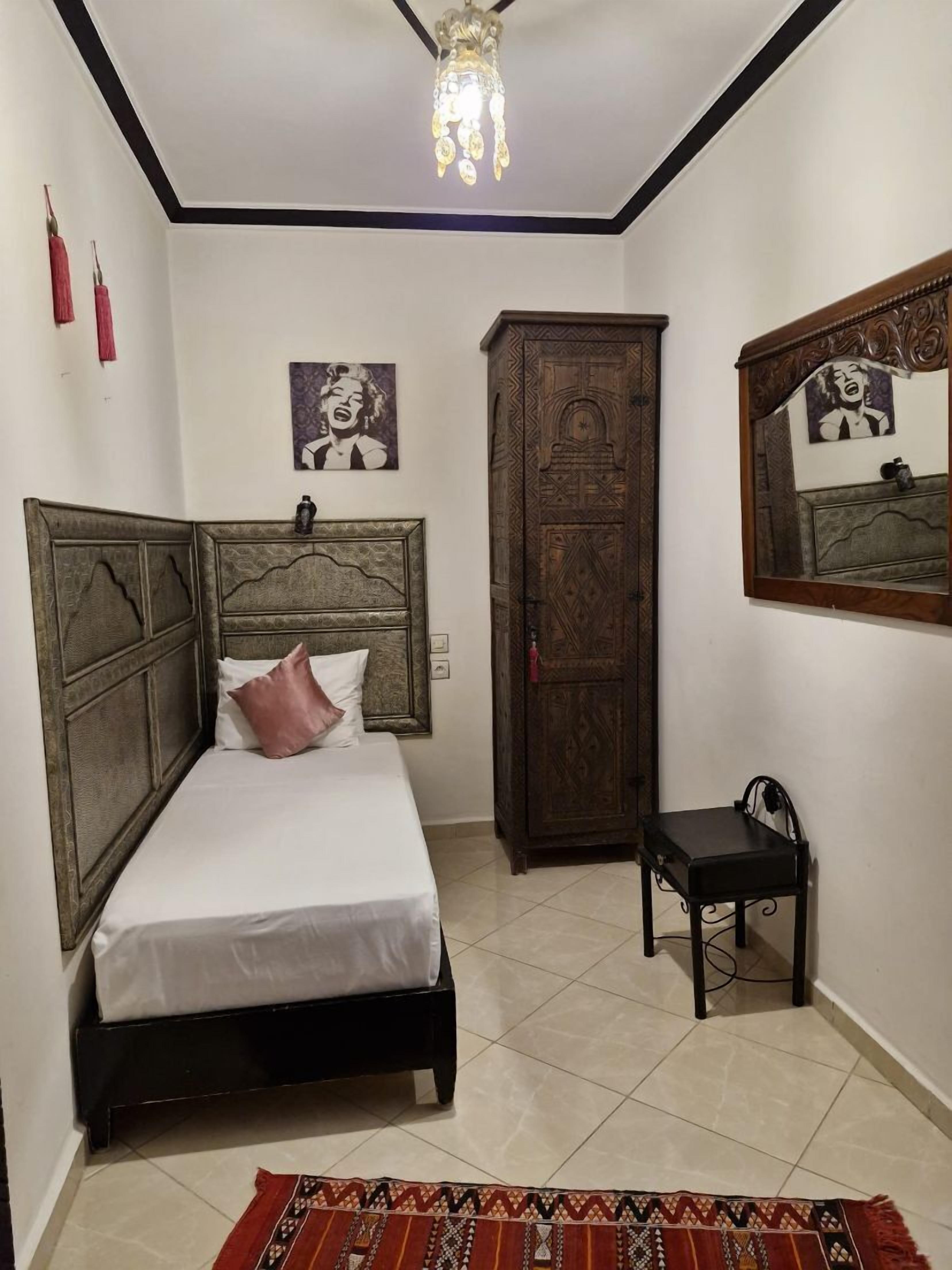 Un dormitorio con cama, armario, una silla y una lámpara colgante.