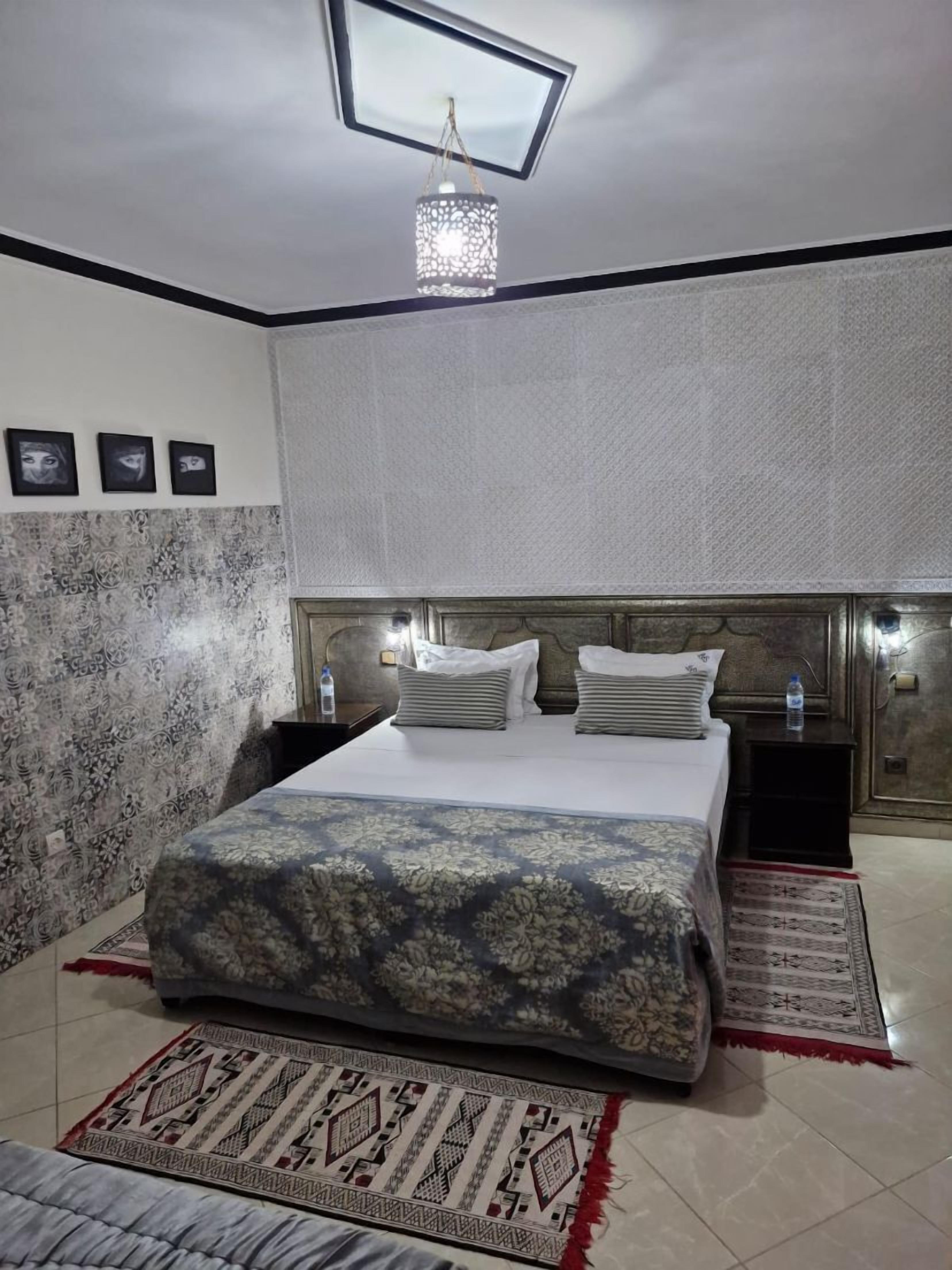 A bedroom with a large bed, a headboard with built-in lighting, a patterned rug, and a ceiling light fixture.