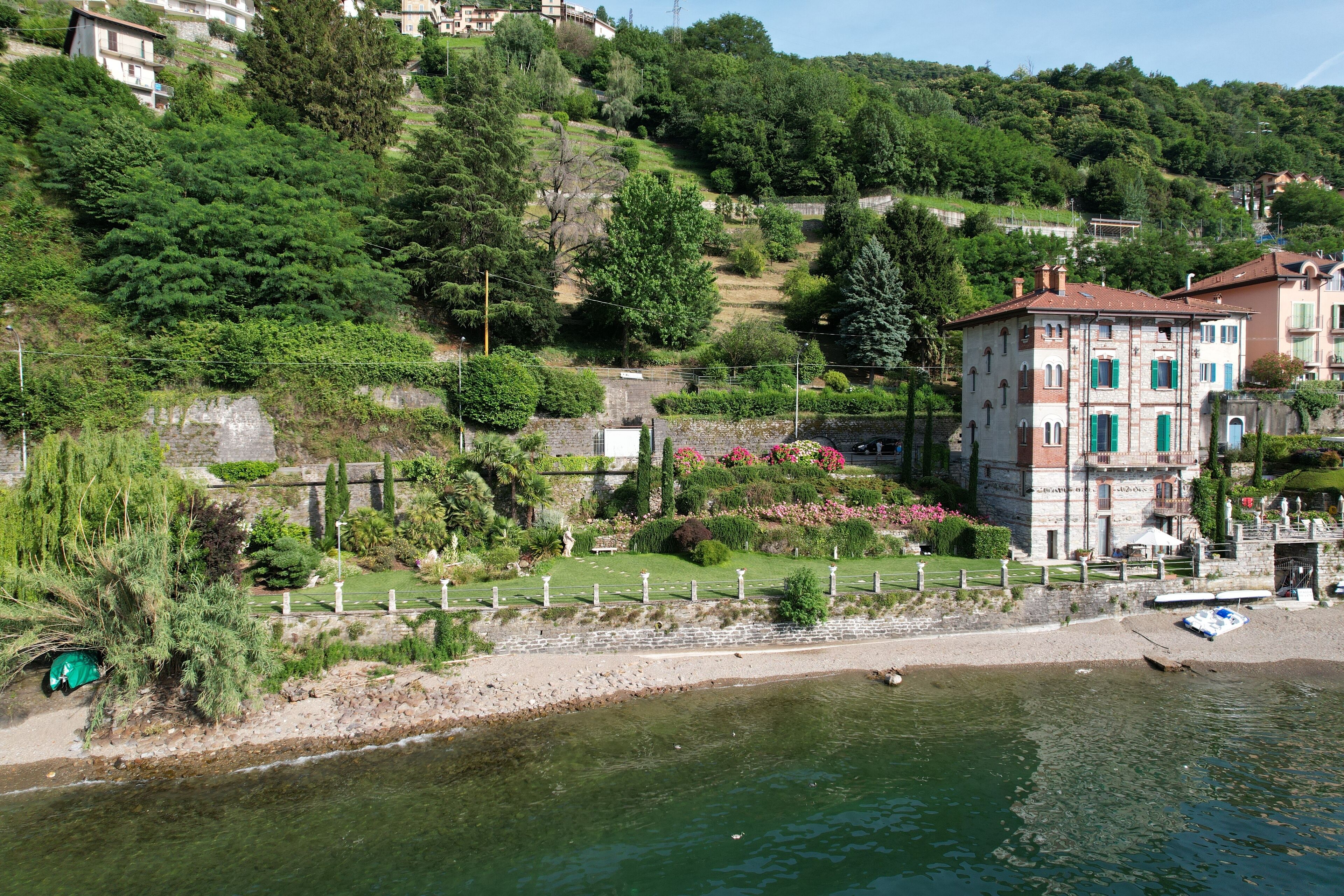 Une vue sur la rivière, avec un bâtiment doté d’une façade en pierre et de volets verts, le tout entouré d’une végétation luxuriante et d’un jardin bien entretenu.