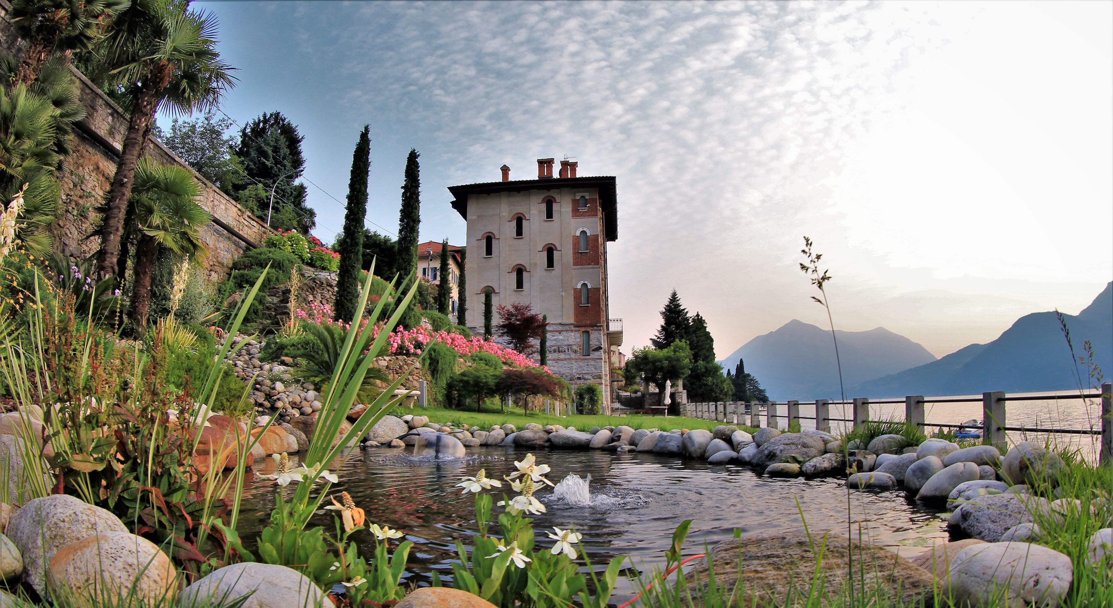 A historic building with a stone facade, a small pond with water lilies, and a mountainous backdrop.