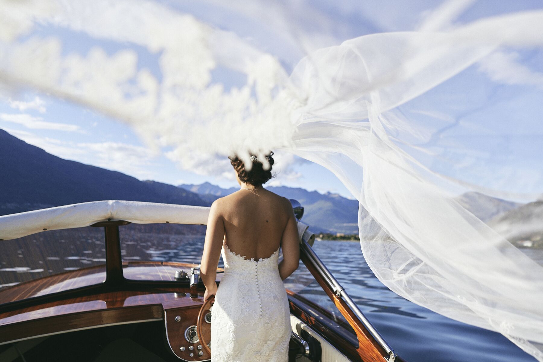 A person in a white dress standing on a boat with a mountainous landscape in the background.