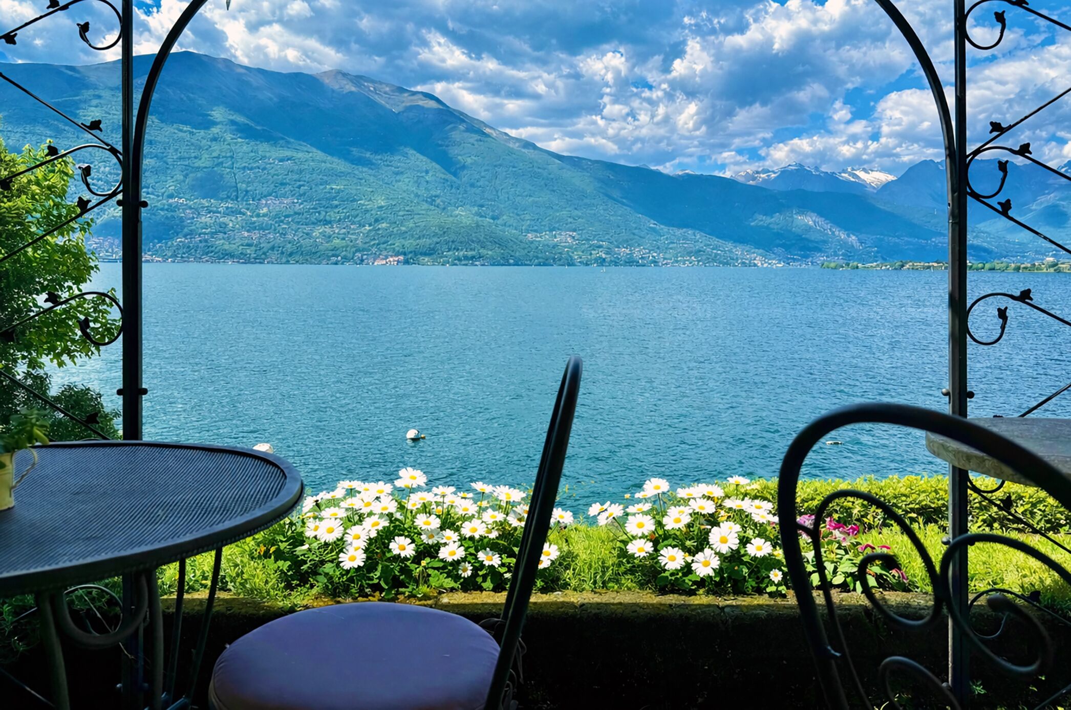 Ein See mit Bergen im Hintergrund, ein Tisch und Stühle im Vordergrund.