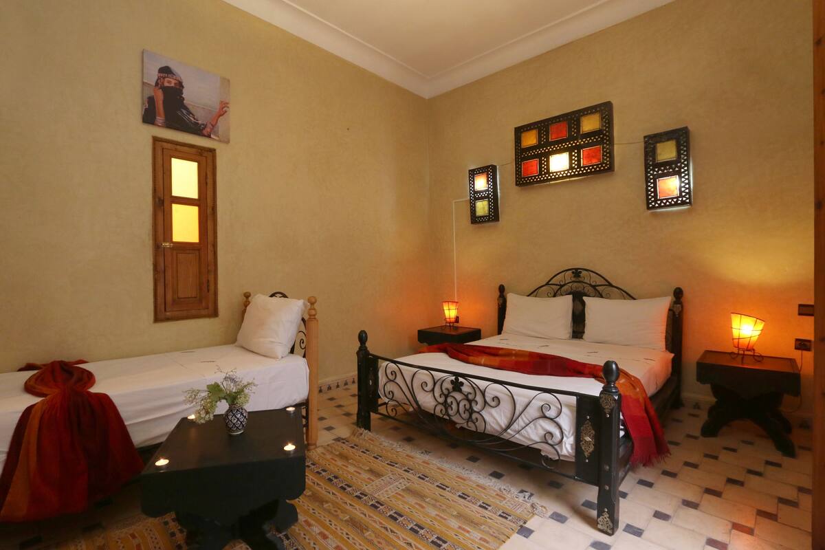 A room with two beds, a wooden door, and decorative wall sconces.