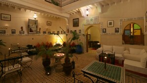 Un amplio salón con techo alto, barandillas ornamentales y una zona de estar con mantel estampado.