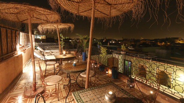 Una terraza al aire libre con sombrillas de paja, suelo de baldosas y mobiliario exterior.