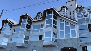 A multi-story building with a stone facade, large windows, and a prominent entrance with steps. - Salta Lake View (San Carlos de Bariloche)