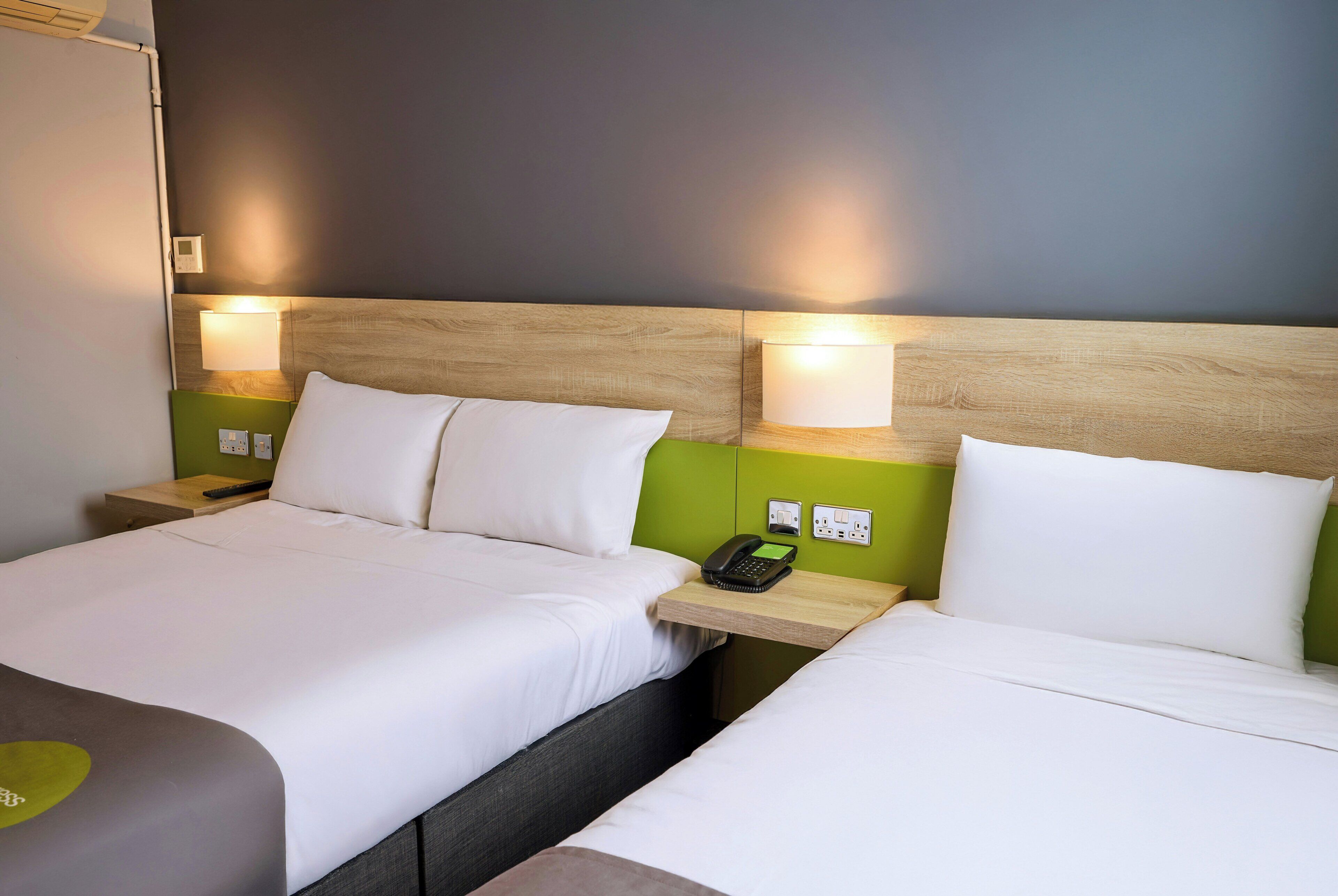 A hotel room with two beds, a bedside telephone, and a green wall.