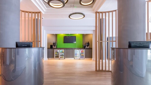 Un espace d’accueil moderne agrémenté d’un mur d’accent vert, d’un téléviseur à écran plat et d’une machine à café.