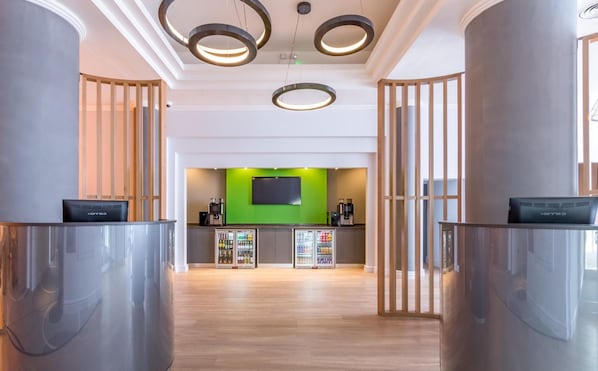 A modern reception area with a green accent wall, a flat-screen TV, and a coffee machine.