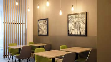 A modern interior with wooden slats, green chairs, and tables, and two framed pictures on the wall.