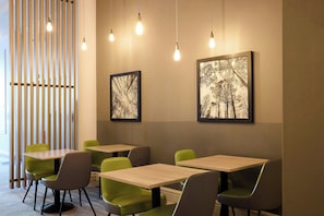 Ein modernes Interieur mit Holzlamellen, grünen Sesseln und Tischen sowie zwei gerahmten Bildern an der Wand.