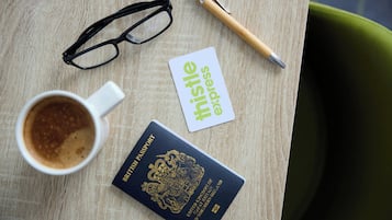 Una mesa con un pasaporte, gafas, un bolígrafo, una tarjeta de presentación y una taza de café.