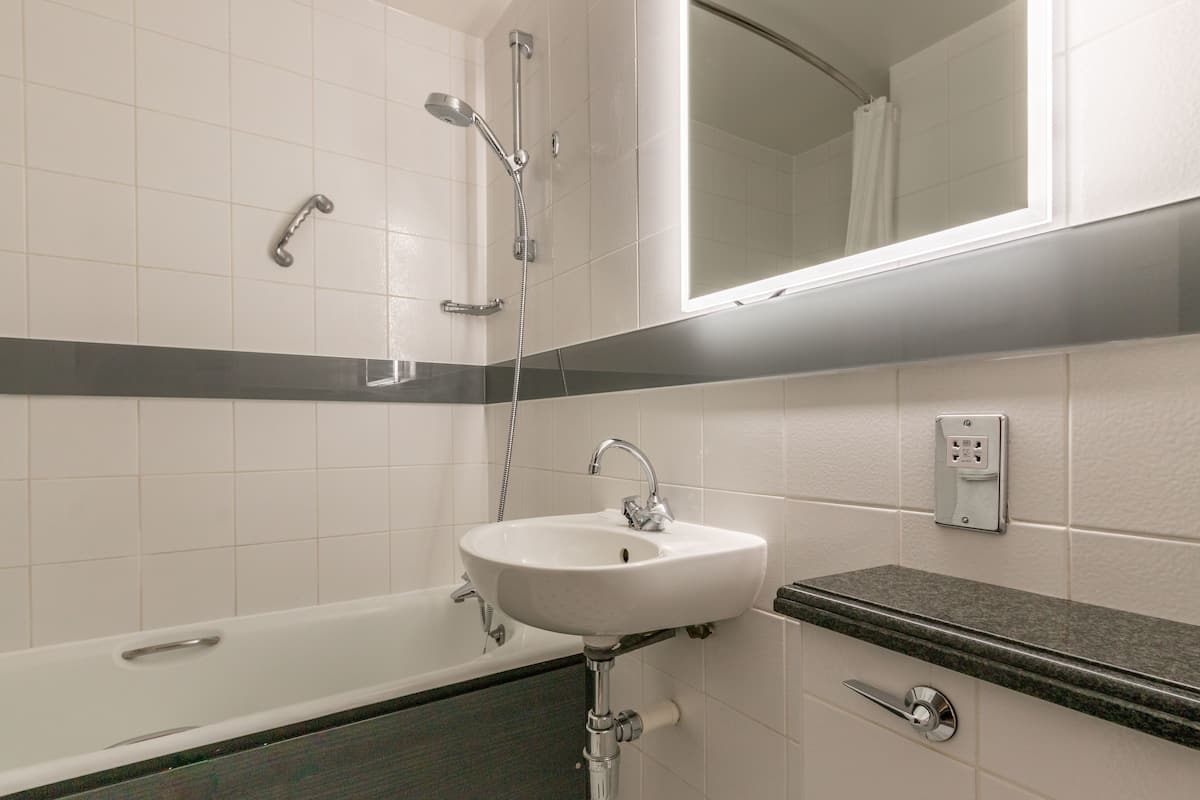 A bathroom with a white sink, a bathtub, a shower, and a mirror above the sink.