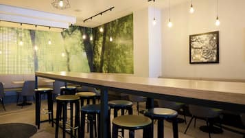 A modern bar area with a long counter, multiple stools, pendant lighting, and a green patterned wall.