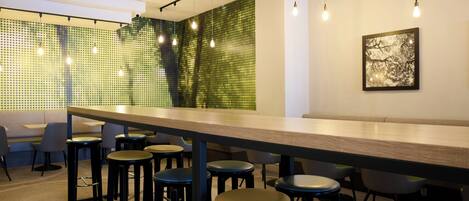 A modern bar area with a long counter, multiple stools, pendant lighting, and a green patterned wall.