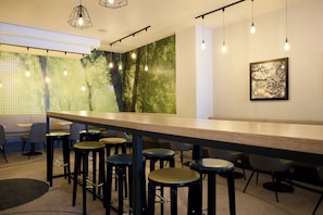 Un espace bar moderne doté d’un long comptoir, de nombreux tabourets, d’un éclairage suspendu et d’un mur orné d’un motif vert.