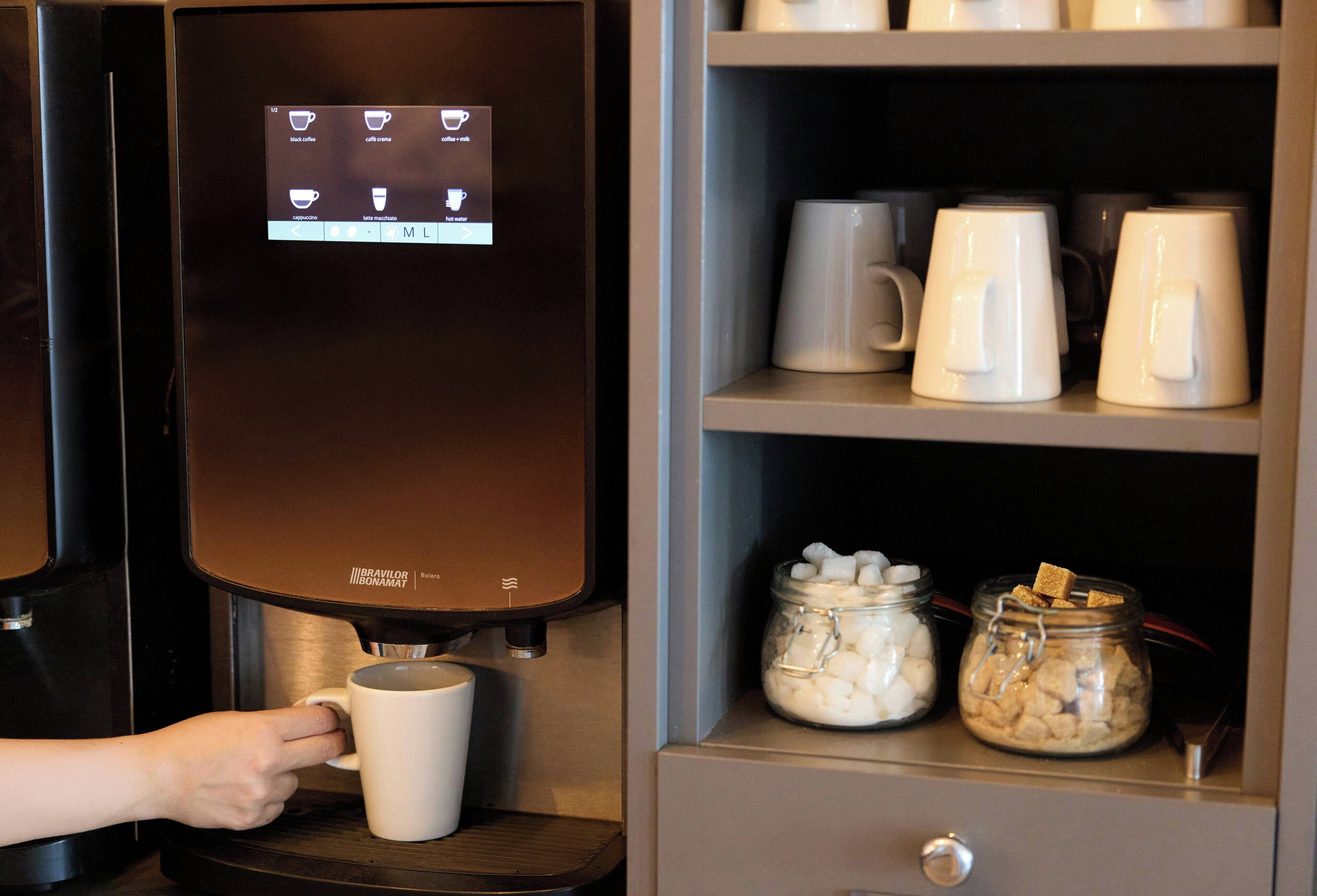 Una máquina de café con pantalla digital y una mano eligiendo una taza.