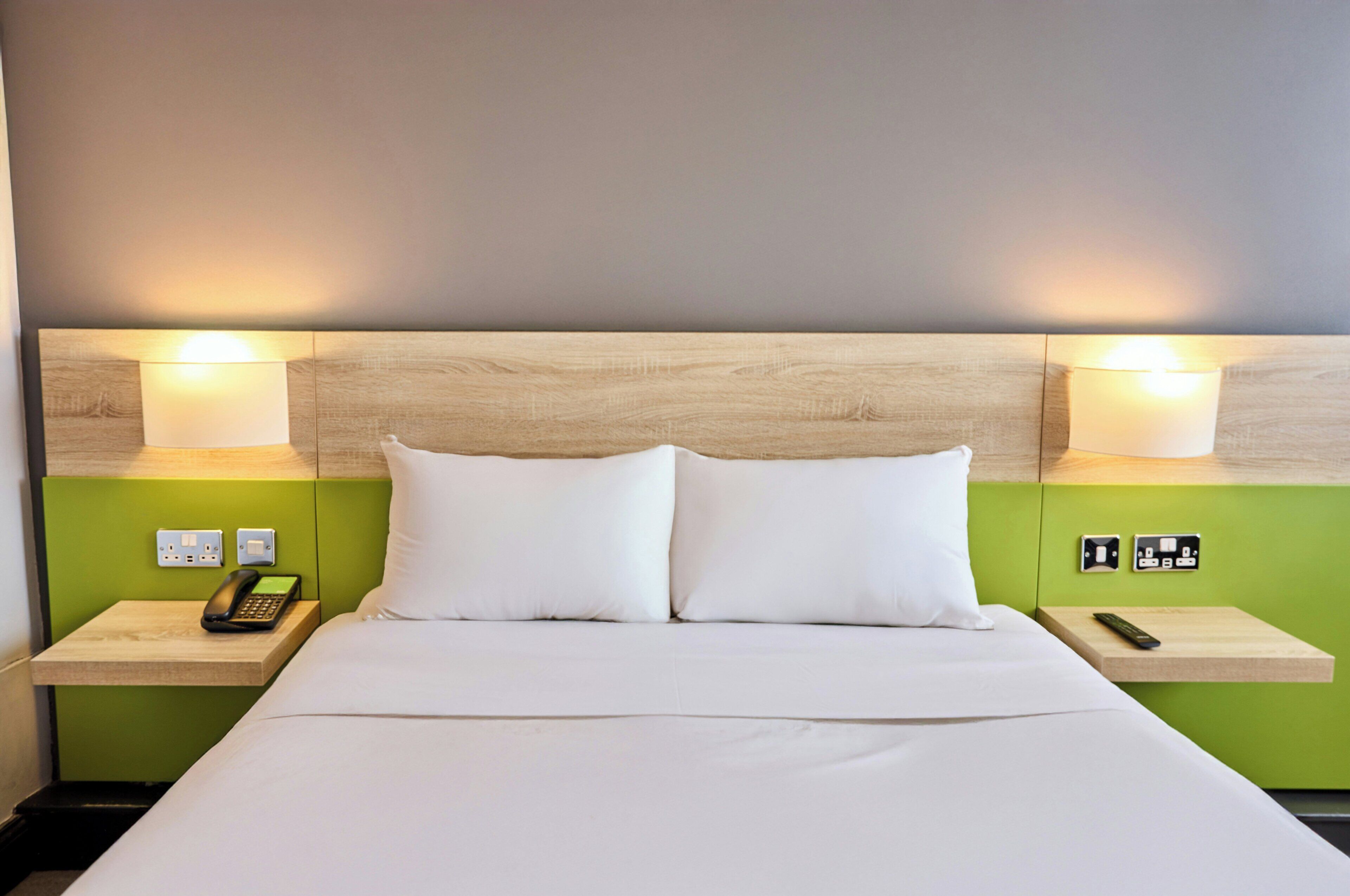 Habitación de hotel con cama, dos mesitas de noche, teléfono e iluminación en la pared.