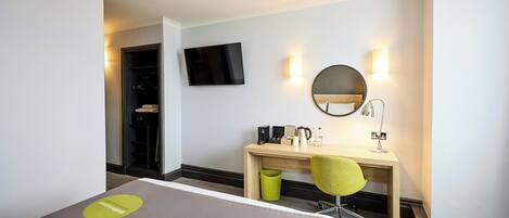 Een hotelkamer met een bed, een bureau met een stoel, een ronde spiegel, een televisie en een kleine prullenbak.