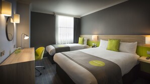 Une chambre d’hôtel avec deux lits, un bureau, une chaise et une fenêtre avec des rideaux.