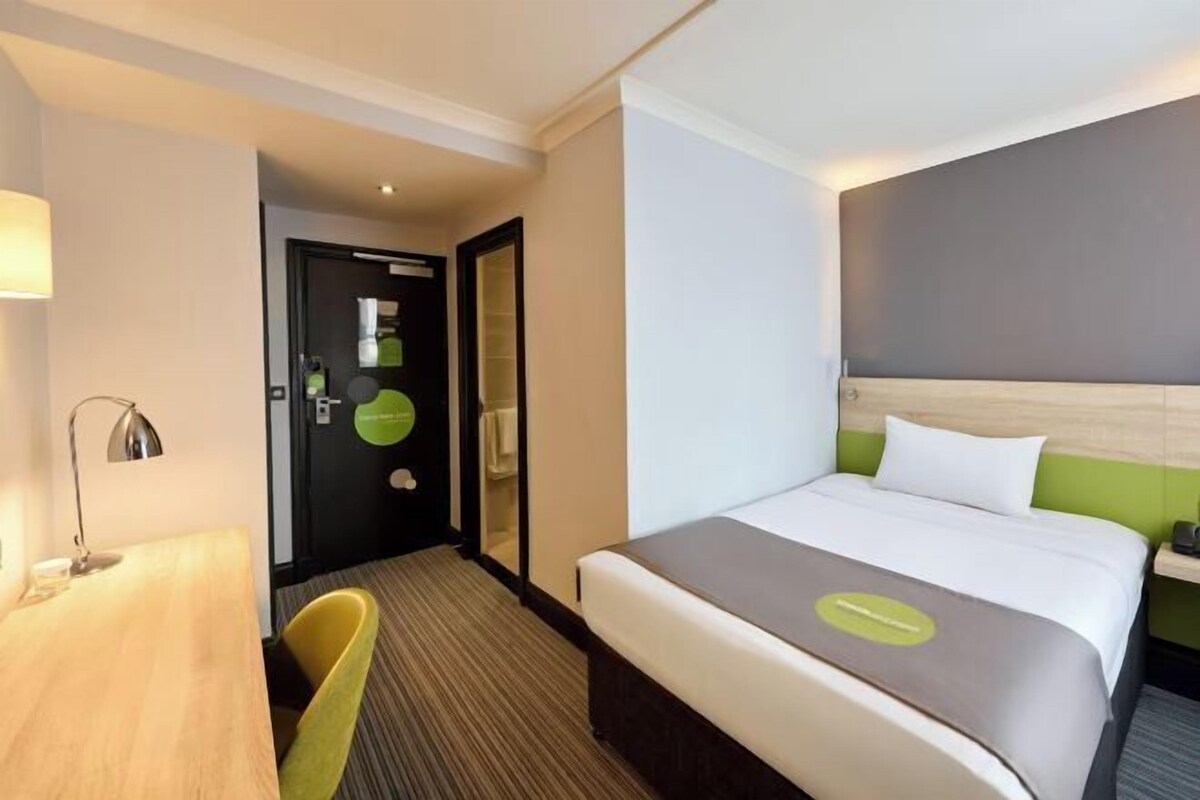 A hotel room with a bed, a desk, a chair, and a door.