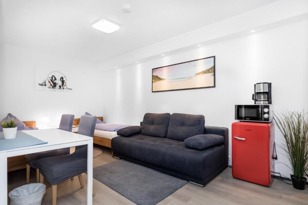 A modern living room with a sofa, a small table, a red refrigerator, and a coffee machine.