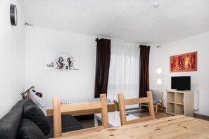 A compact living space with a bed, a sofa, a small table, a TV, and a painting on the wall. - Pension Genat (Wedemark)