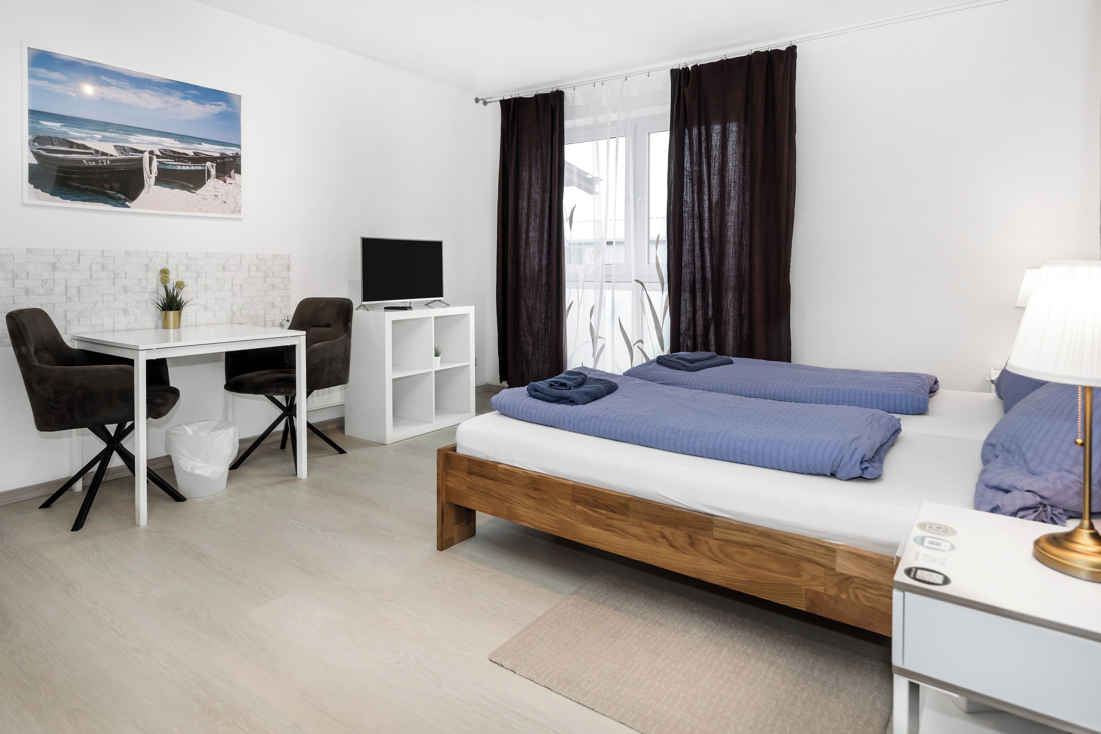 A modern hotel room with a wooden bed, a desk, a chair, a TV, and a window with curtains.