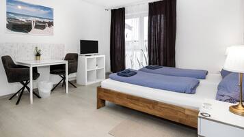 A modern hotel room with a wooden bed, a desk, a chair, a TV, and a window with curtains.