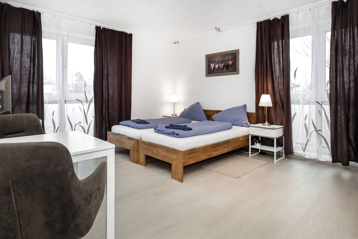 A modern hotel room with a wooden bed, two bedside tables, a desk, and a chair.