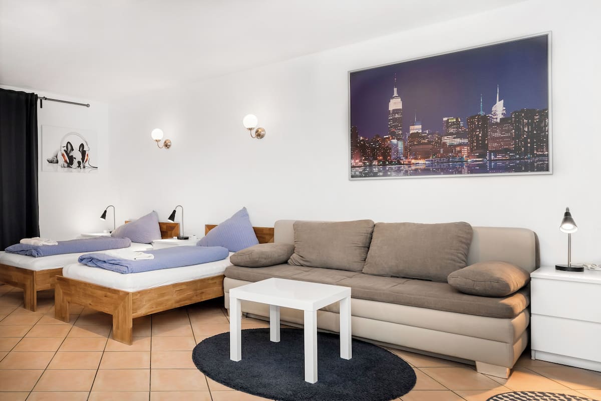 A modern living room with a sofa, two beds, a coffee table, and a cityscape painting.