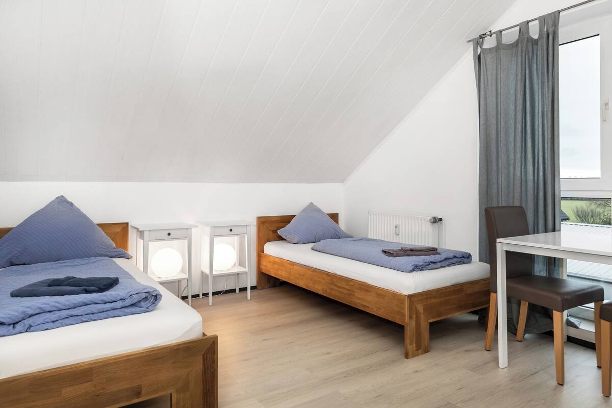 A room with two wooden beds, a small table, and a chair.