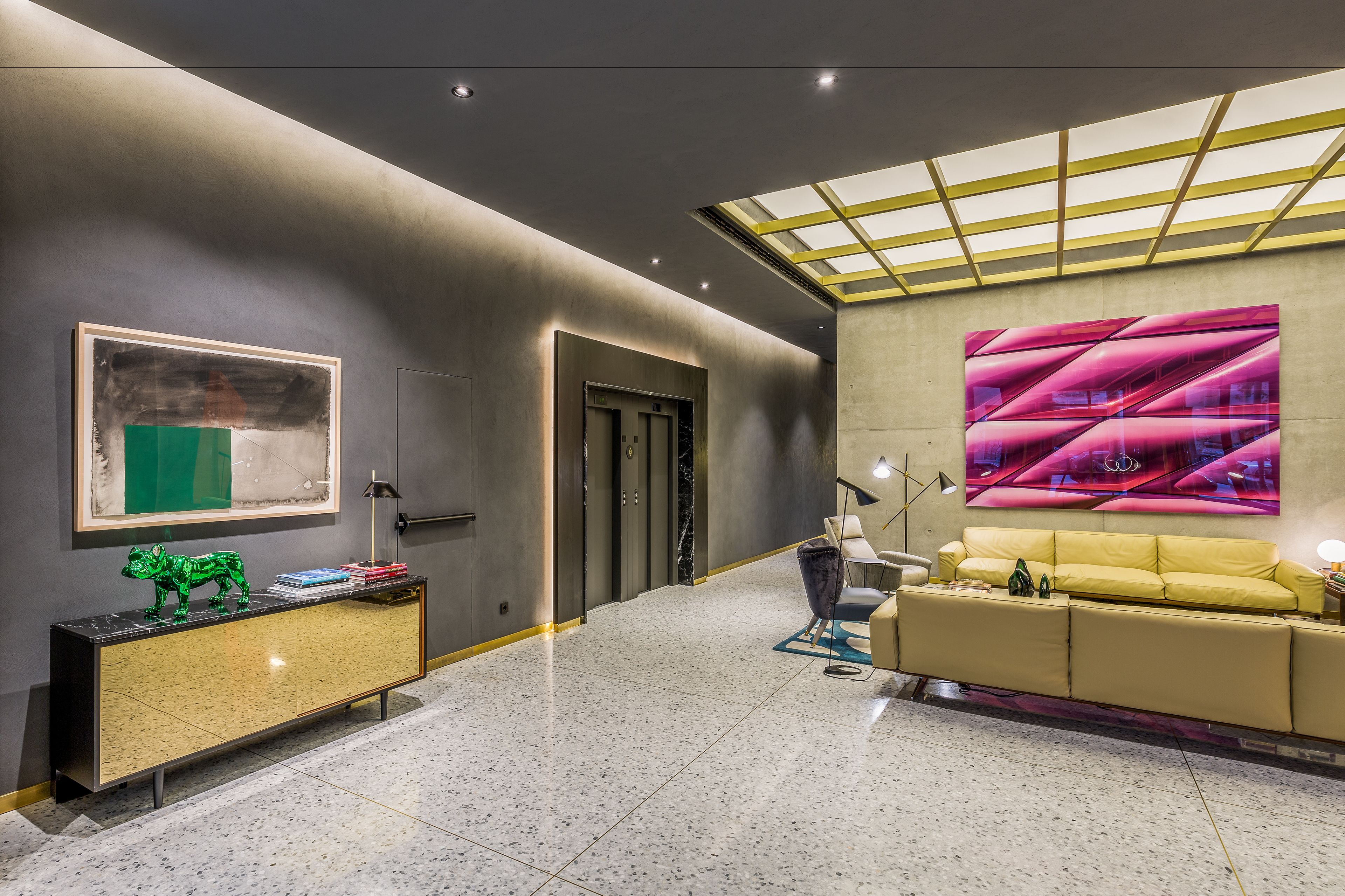 Een moderne lobby met een marmeren vloer, een gele bank, een groene sculptuur en een groot abstract schilderij.