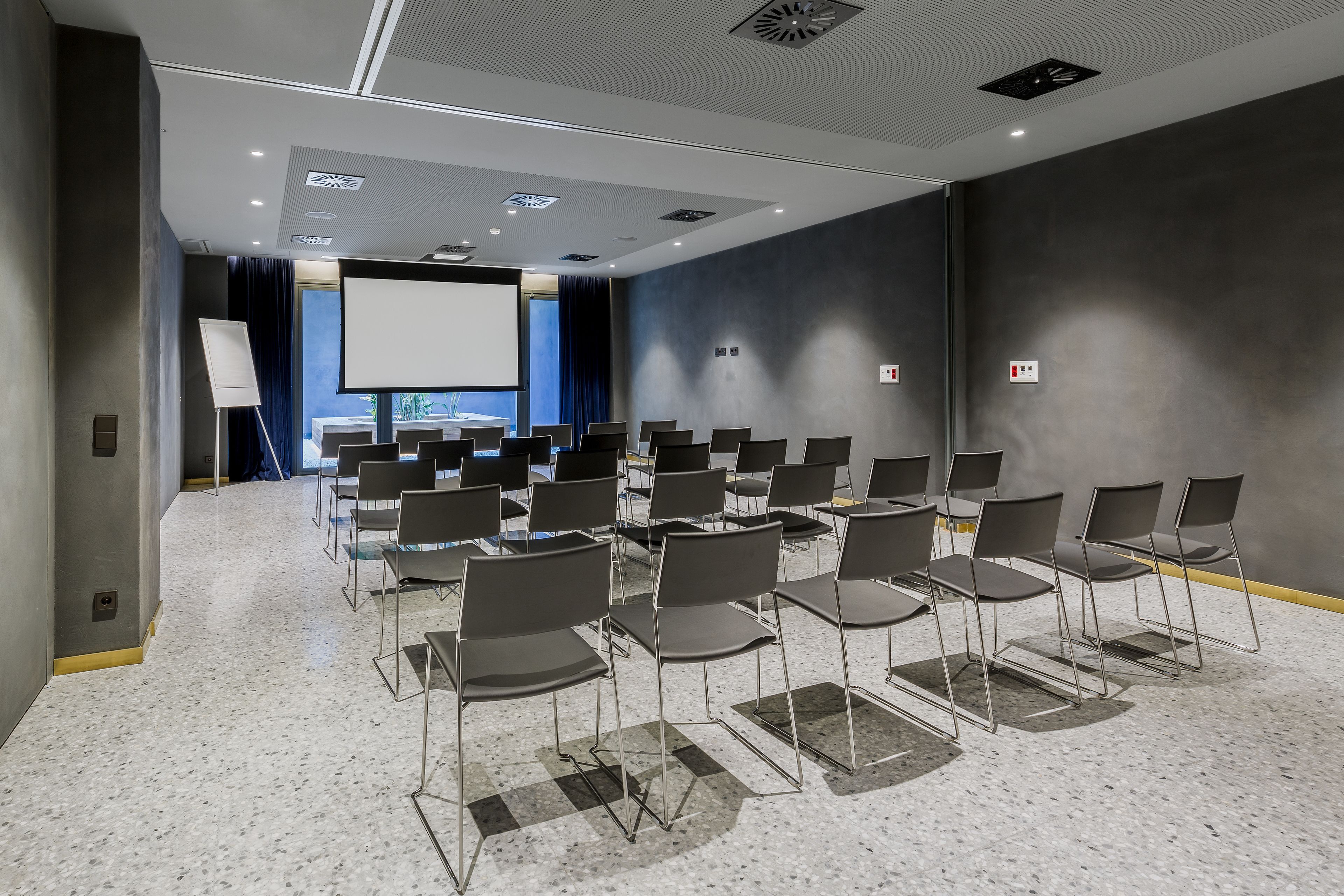 A conference room with rows of chairs, a projector screen, and a large window with curtains.