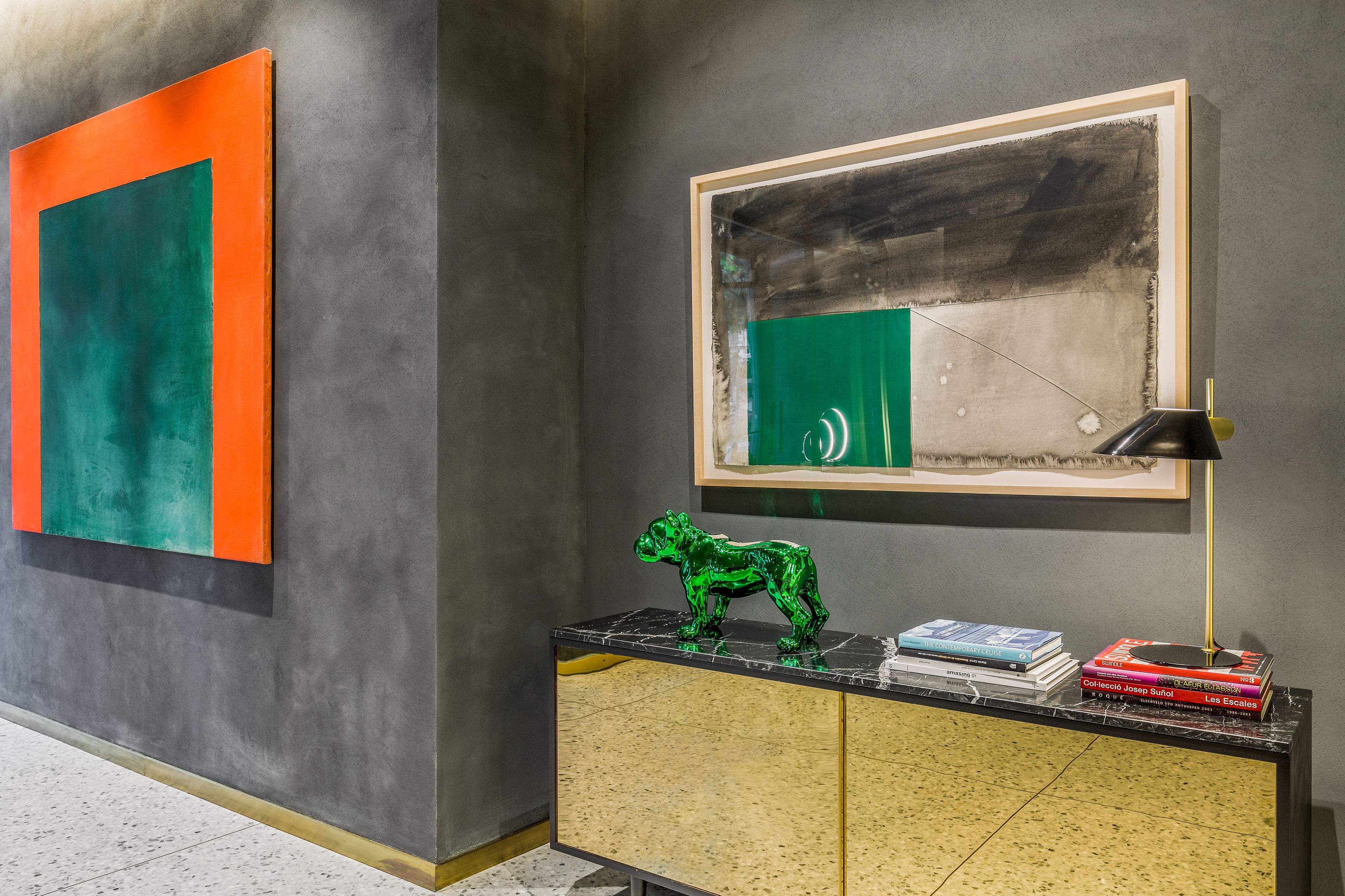 Un interior moderno con un cuadro abstracto grande, una escultura y una pila de libros sobre una consola.