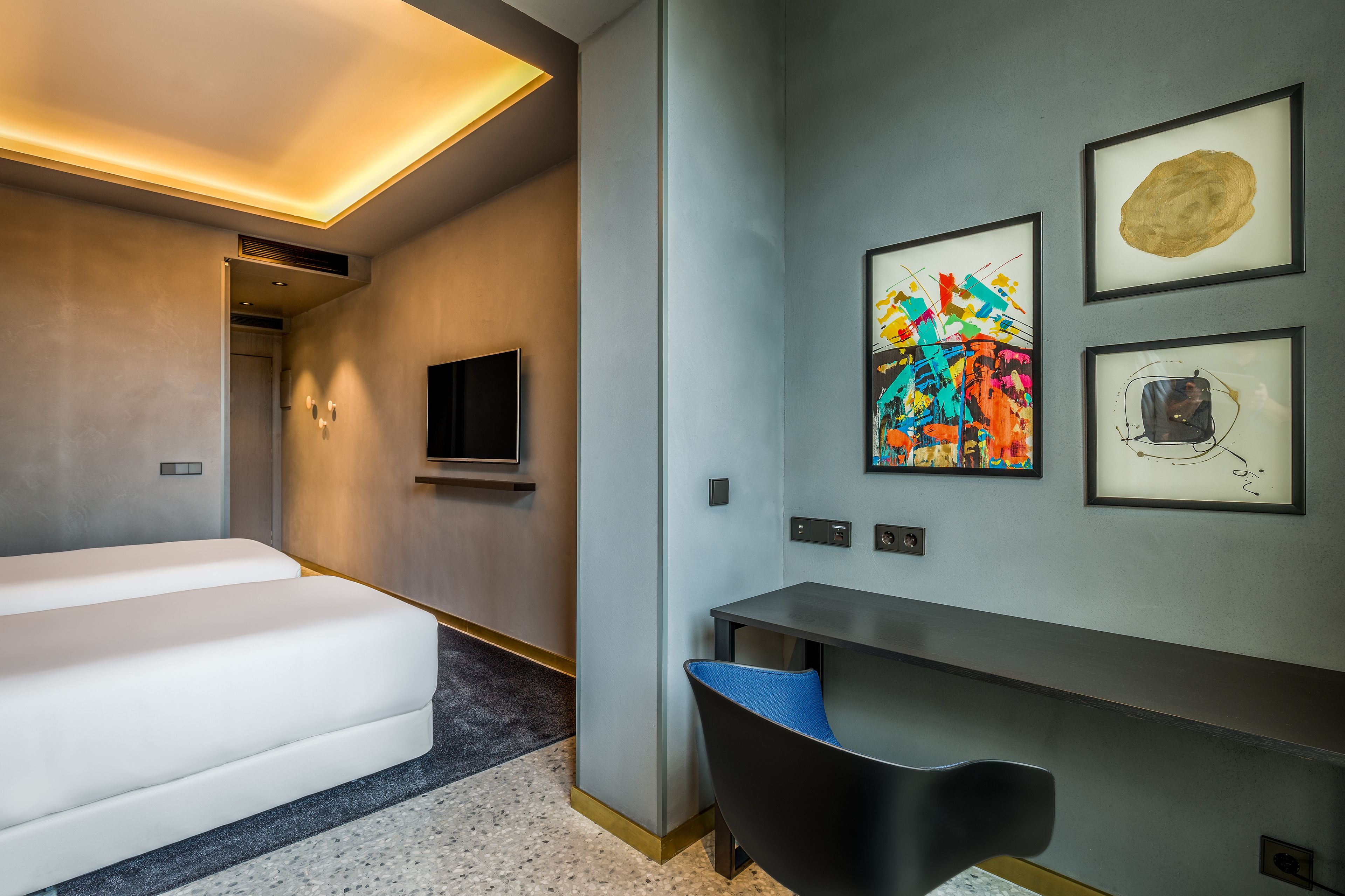 Quarto de hotel moderno com cama, escrivaninha e televisão.