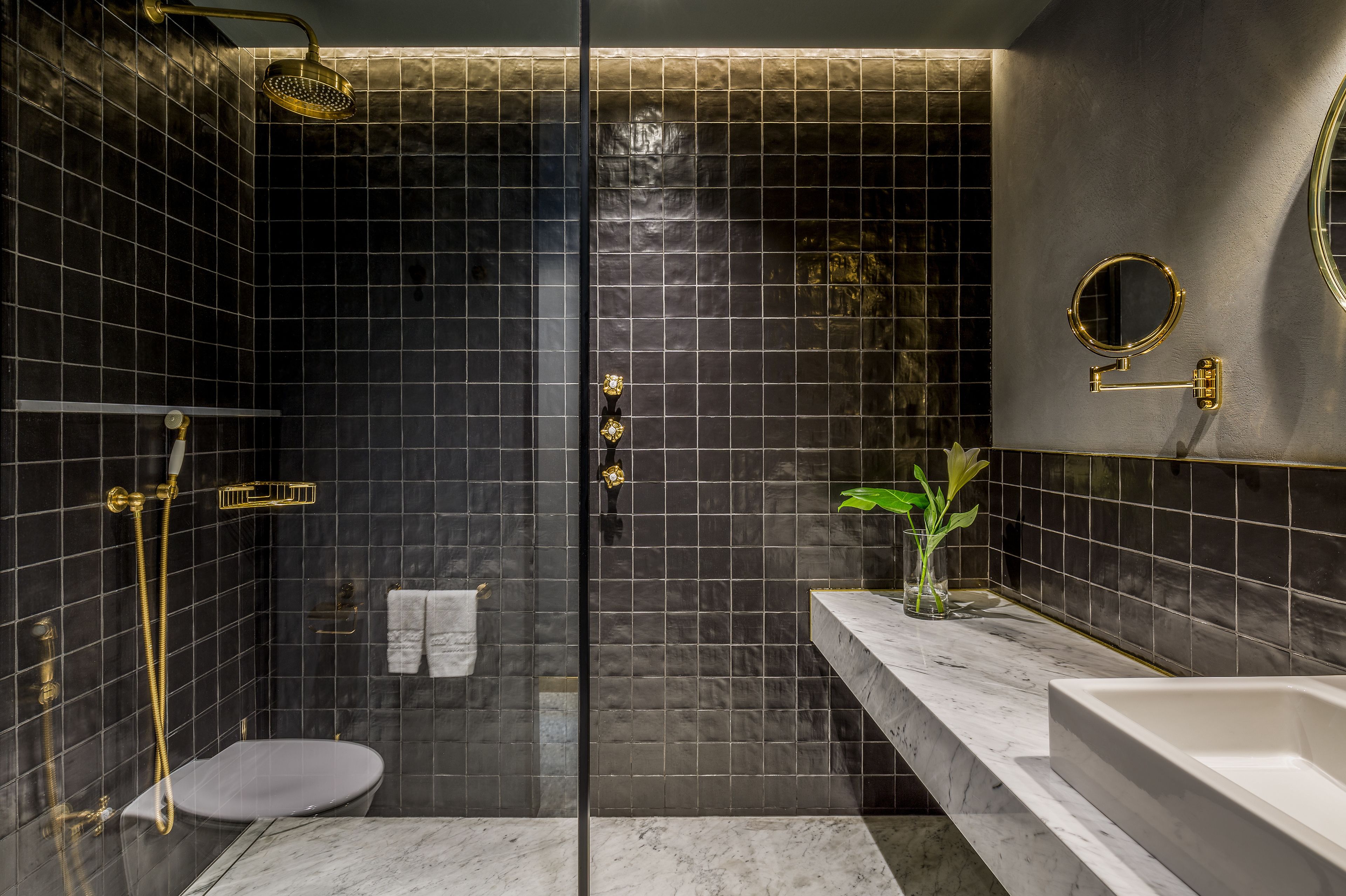 A modern bathroom with a glass-enclosed shower, a white toilet, a marble countertop, and a gold-framed mirror.
