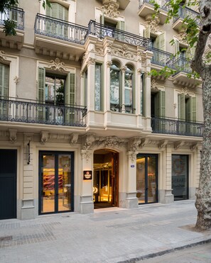 Fachada de hotel com detalhes arquitetônicos elaborados, grandes janelas de vidro e entrada imponente.
