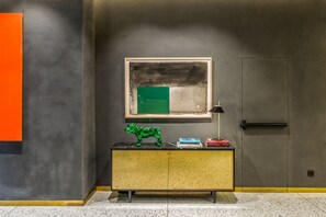 A modern room with a marble floor, a wooden cabinet with a green sculpture, a framed abstract painting, and a door with a handle.