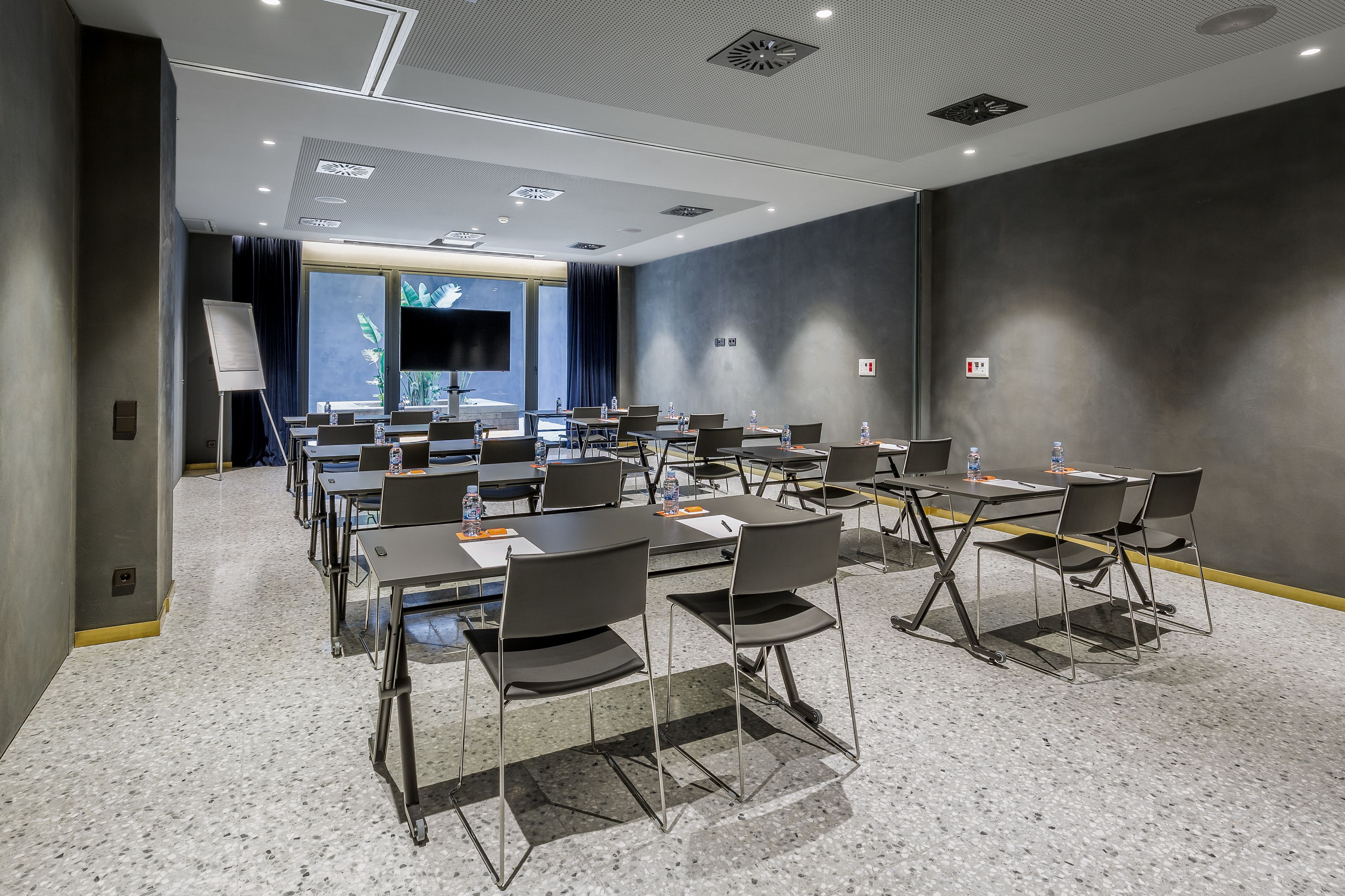 A conference room with multiple tables and chairs, a whiteboard, and a large window with a view of greenery.