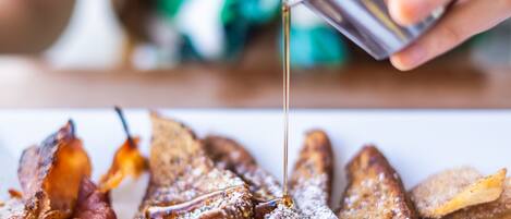 Une assiette de petit-déjeuner comprenant des tranches de pain perdu, du bacon et du sirop.