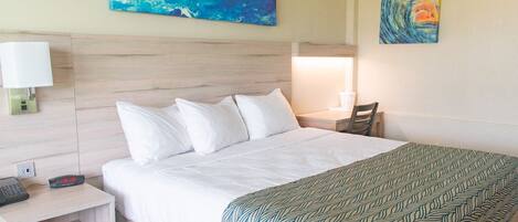A hotel room with a bed, a nightstand with a phone and lamp, and two paintings on the wall.