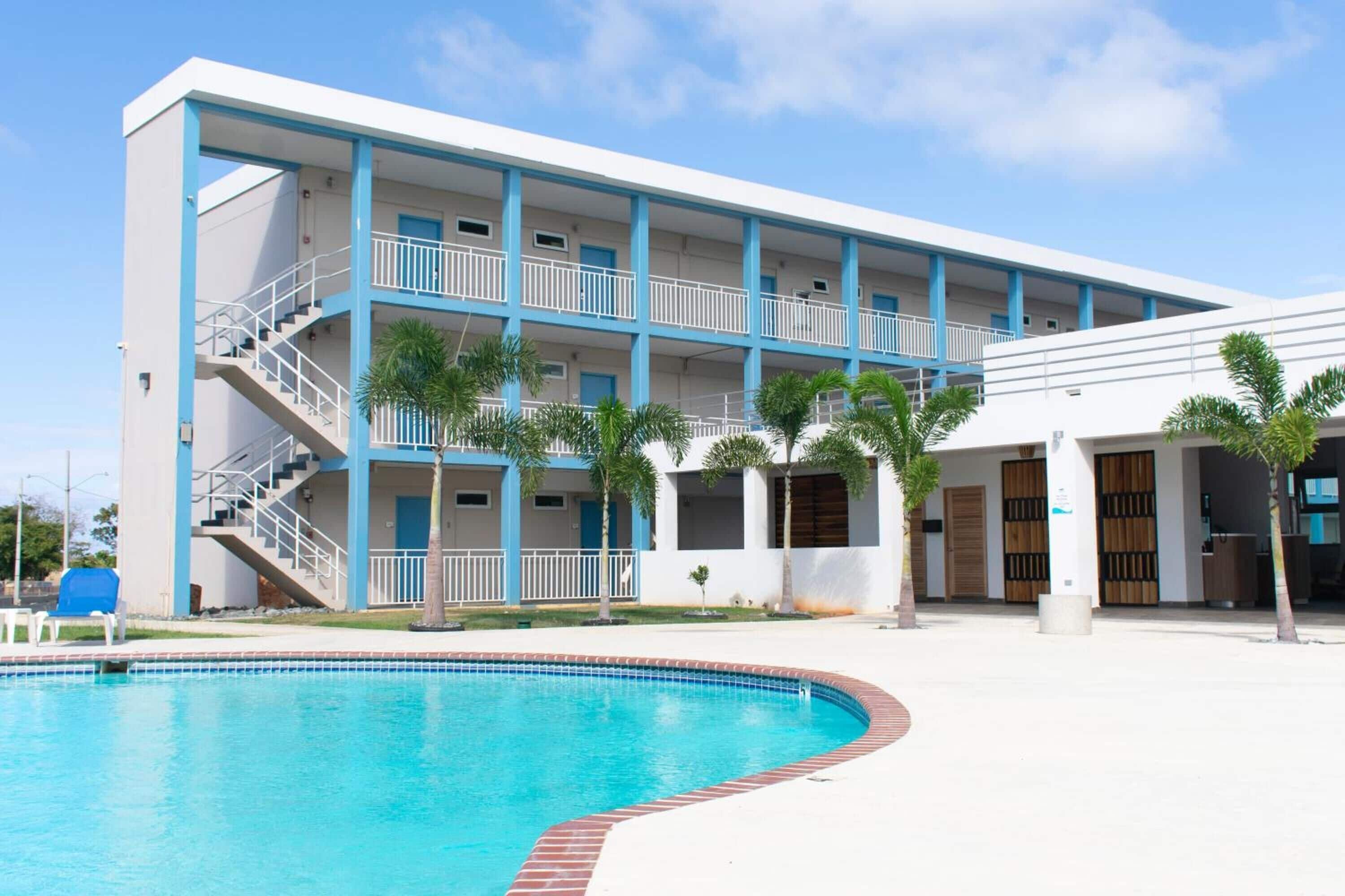 Un hotel de varios pisos con piscina, balcones y palmeras.