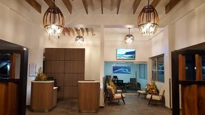 A reception area with wooden reception desks, a TV screen, and a seating area with chairs and a table. - Punta Borinquen Resort (Aguadilla)