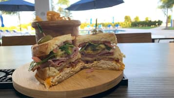 Un sándwich sobre una tabla de madera en una mesa al aire libre, con sombrillas al fondo.