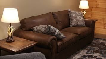 A brown leather sofa with patterned cushions, two wooden side tables with lamps, and a wooden wall with a picture frame.