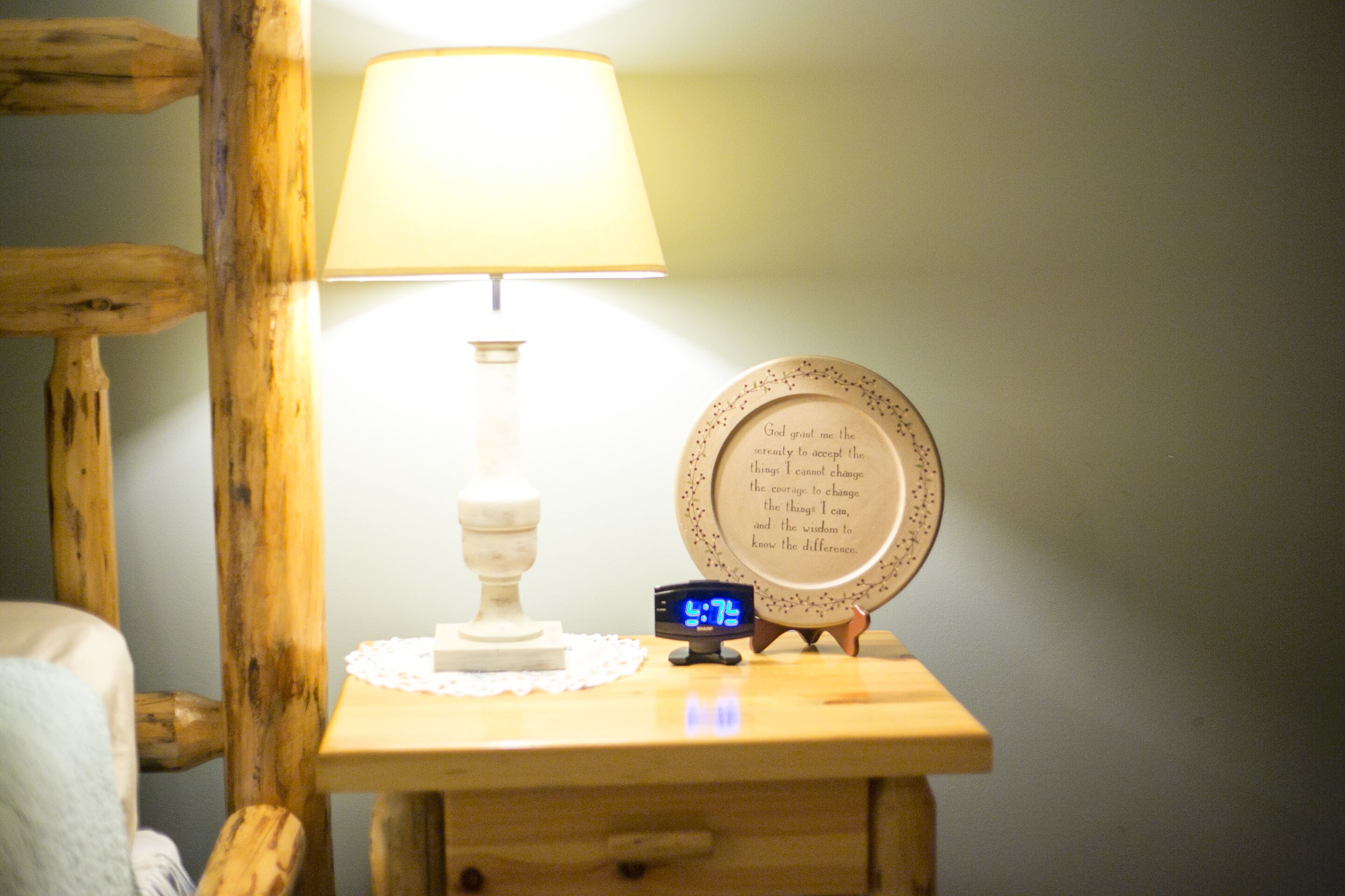 A bedside table with a lamp, a clock, and a decorative plate with text.