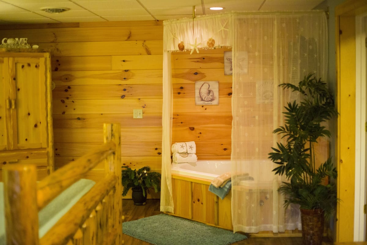 A wooden cabin interior with a wooden bench, a bathtub, and potted plants.